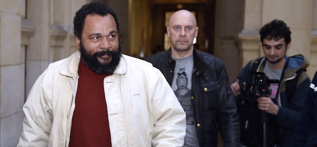 French controversial comic Dieudonne M'bala M'bala (L) and French far-right writer Alain Soral (C) arrive at the Paris courthouse on March 12, 2015, for Soral's trial for posting a picture of himself on the internet taken in Berlin in front of the Memorial to the Murdered Jews of Europe, while gesturing the "quenelle", a gesture viewed as anti-Semitic. The gesture, invented by French controversial comic Dieudonne M'bala M'bala, is viewed as anti-semitic, while Dieudonne and his supporters claim it is anti-establishment. AFP PHOTO / LOIC VENANCE (Photo credit should read LOIC VENANCE/AFP/Getty Images)
