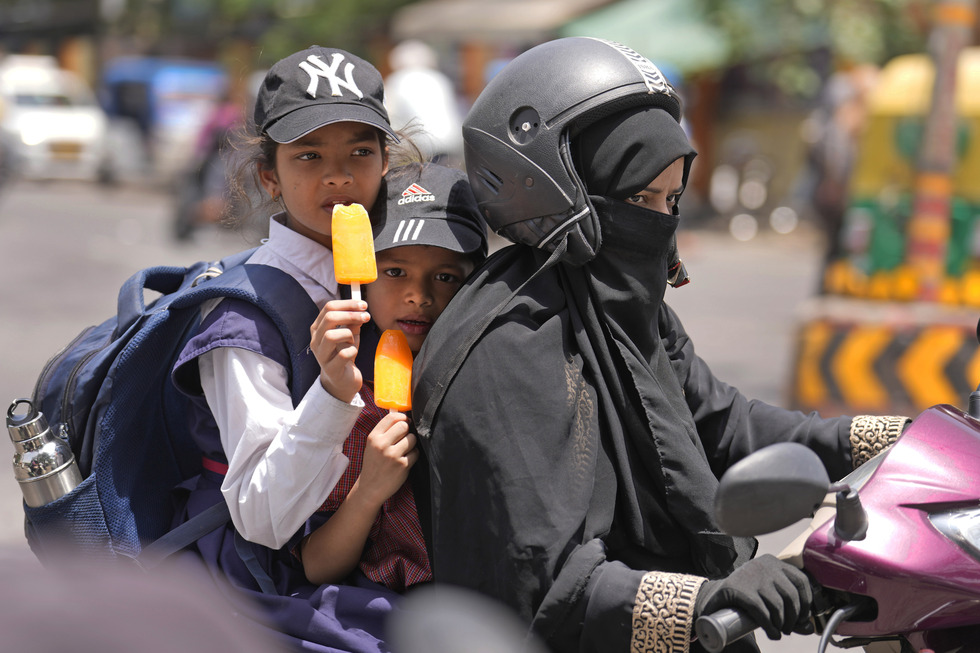 Due bambini mangiano un ghiacciolo mentre vengono portati a scuola dalla madre, durante la grande ondata di calore che da giorni colpisce vari paesi del sudest asiatico (AP Photo/Rajesh Kumar Singh)