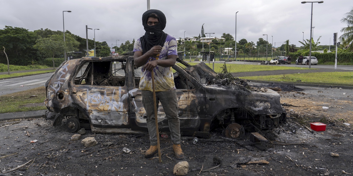 Un uomo davanti ad una macchina bruciata a Nouméa, la città principale della Nuova Caledonia