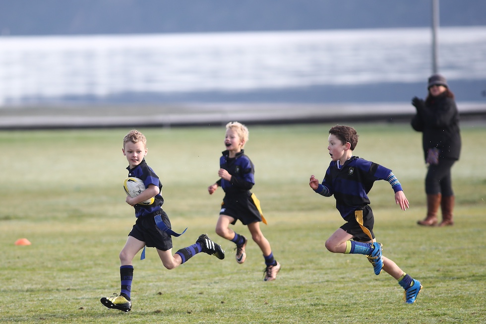 Tre ragazzini in divisa da rugby corrono su un campo da gioco