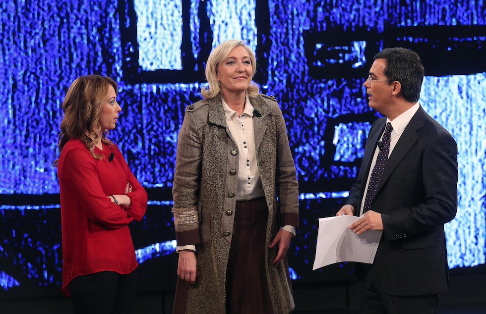 Da sinistra a destra: Giorgia Meloni, vestita di rosso; Marine Le Pen, con un cappotto grigio; e il conduttore televisivo Giovanni Floris negli studi della trasmissione "Di Martedì" nel 2015