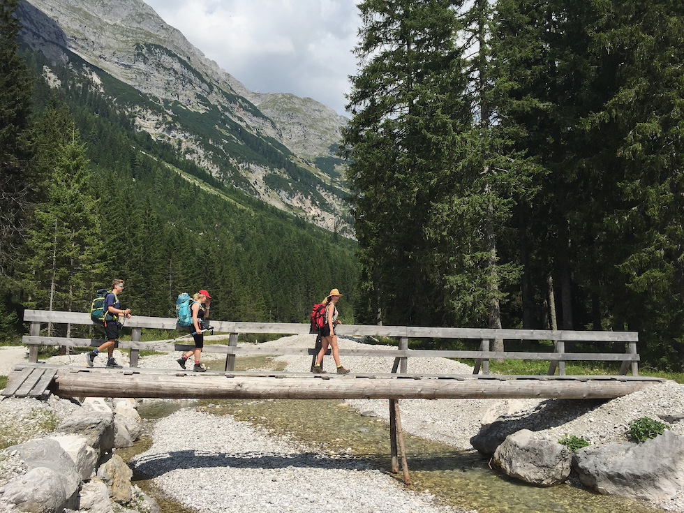 Tre persone percorrono un ponte di legno sospeso su un torrente