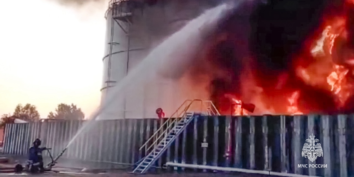 Un vigile del fuoco in ginocchio sulla sinistra tira acqua contro un incendio, a destra