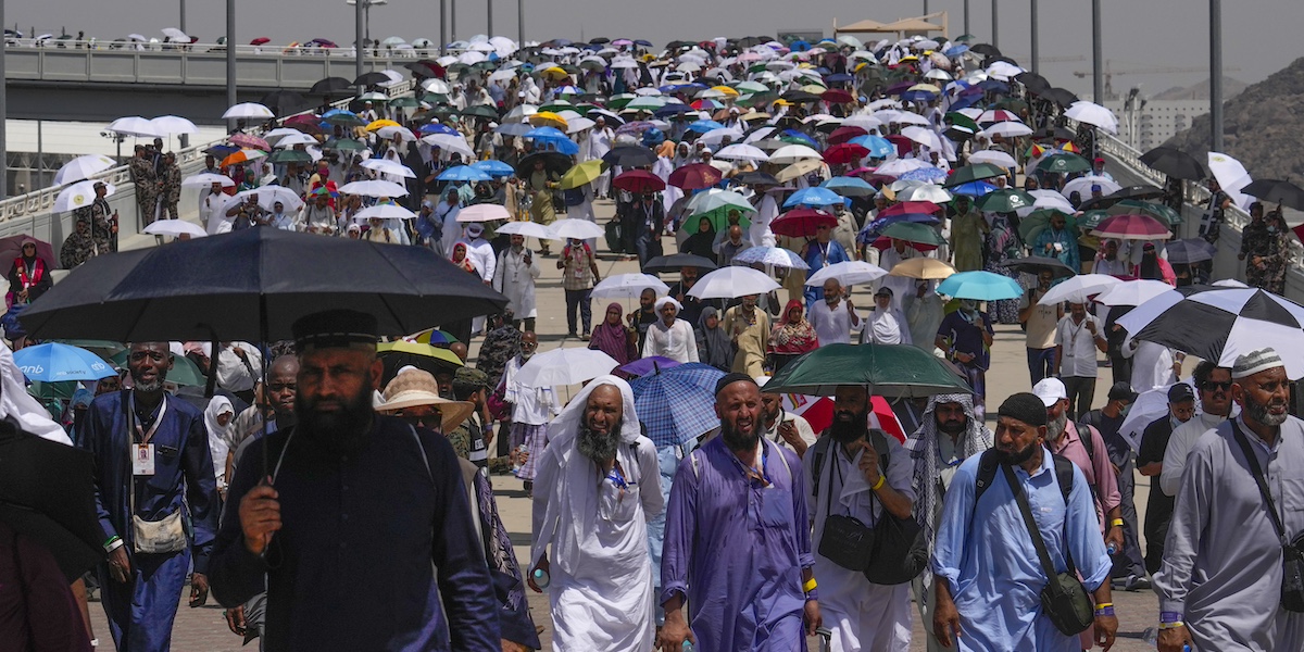 una folla di persone con tuniche lunghe e ombrelli in una strada assolata