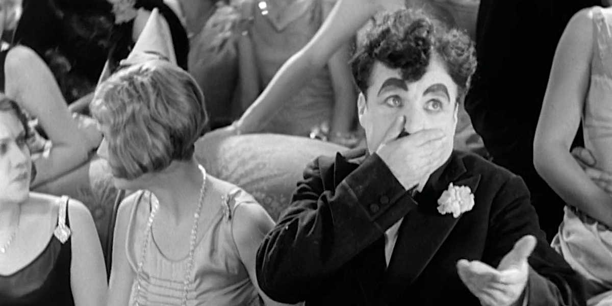 Charlie Chaplin si tiene una mano sulla bocca in una scena in cui ha il singhiozzo dopo aver ingoiato un fischietto