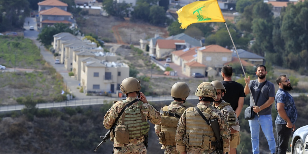 Soldati libanesi e un uomo con la bandiera di Hezbollah al confine con la città di Metula, in Israele (AP Photo/Mohammed Zaatari)
