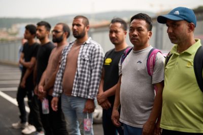 Foto di persone migranti in fila, in primo piano