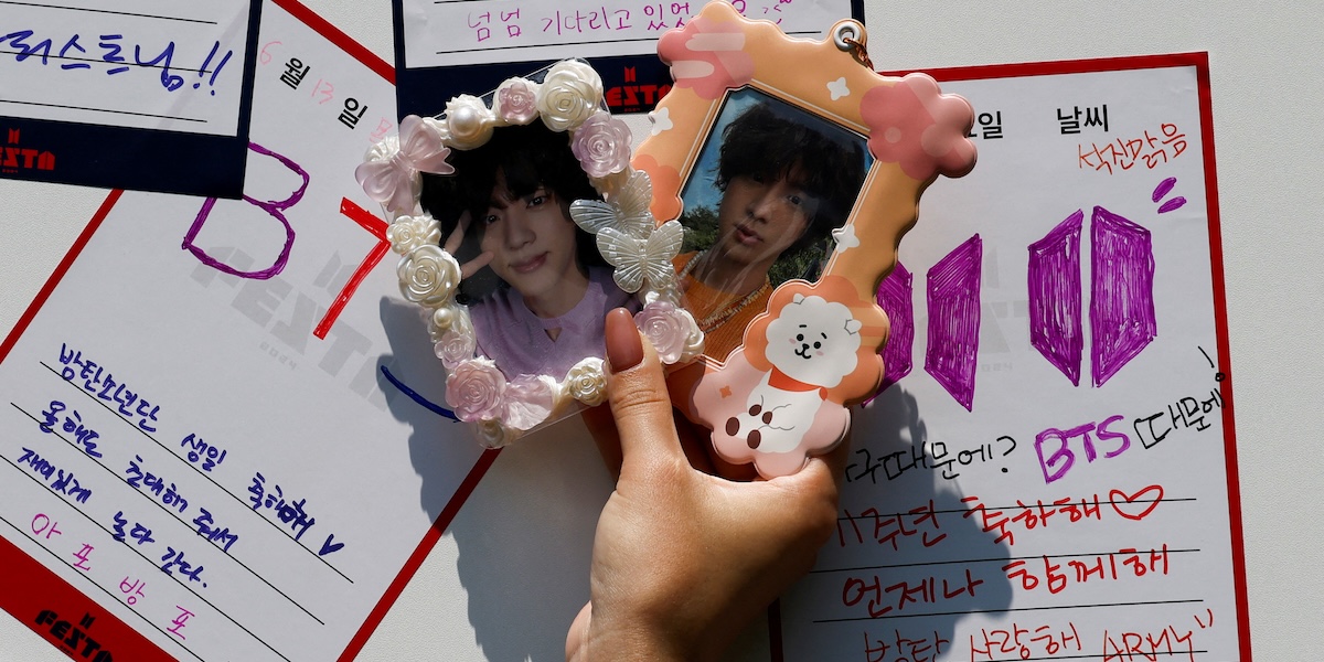 Una ragazza mostra due foto di Jin dei BTS durante un evento per fan della celebre band k-pop a Seul, Corea del Nord, 13 giugno 2024