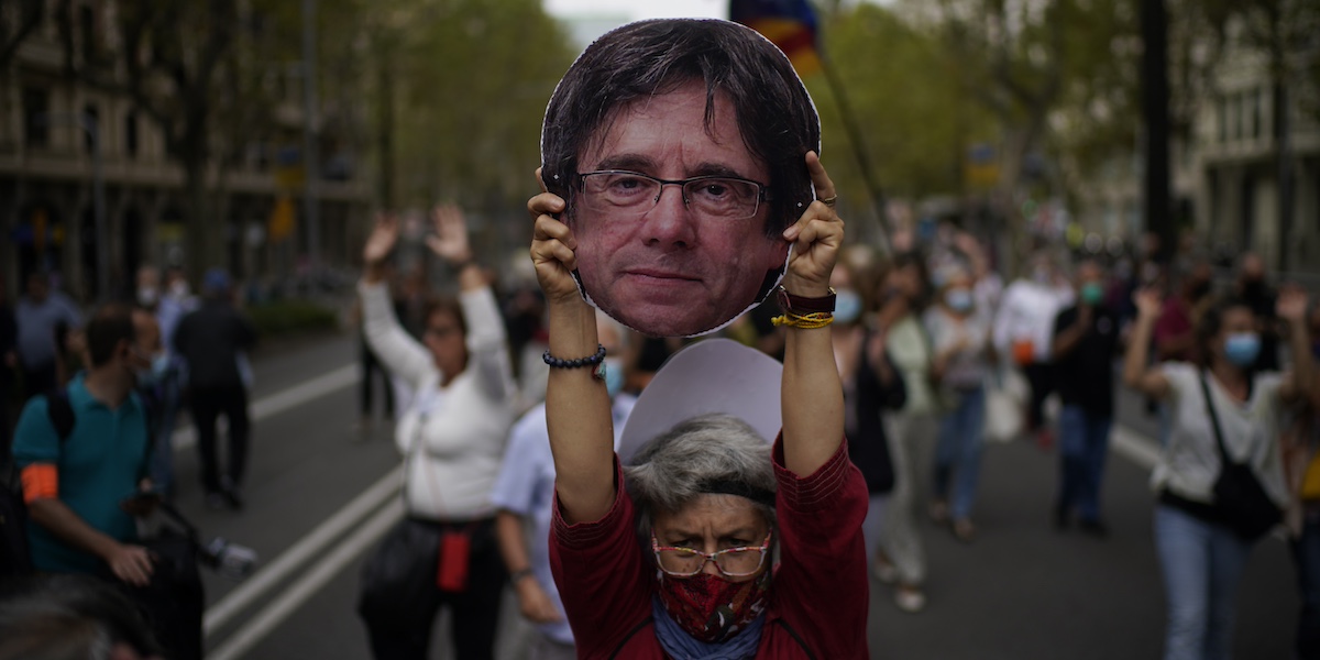 Una donna tiene in mano una maschera con la faccia di Carles Puigdemont durante una protesta a Barcellona, nel 2021 (AP Photo/Joan Mateu)