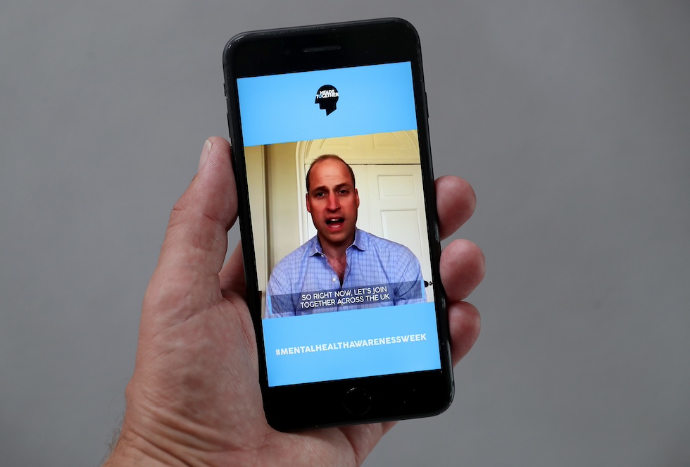 Una mano regge uno smartphone che mostra il principe William in videochiamata 