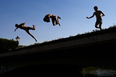 Tre ragazzi si tuffano in un laghetto della città, dove in questi giorni le temperature hanno superato i 39 °C. La foto è di martedì.