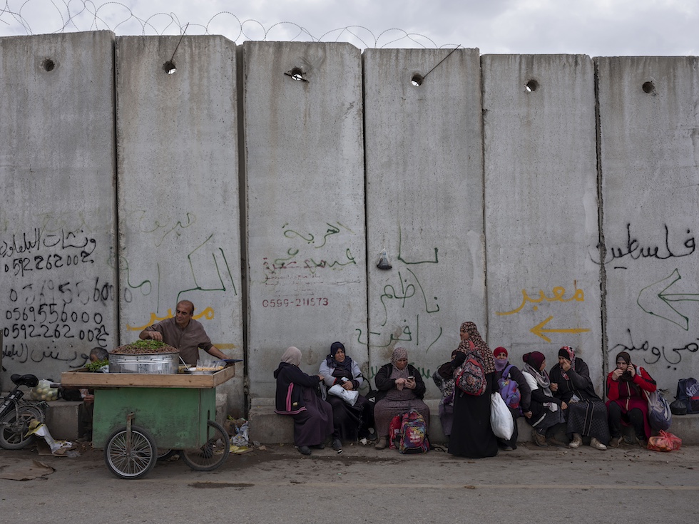 Una foto di un gruppo di palestinesi nella città di Qalqilya che siede accanto al muro che Israele ha fatto costruire in Cisgiordania a partire dai primi anni del Duemila (AP Photo/Oded Balilty)