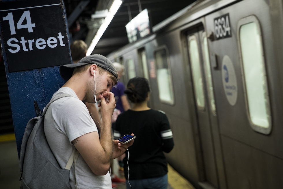 Un ragazzo osserva un filmato sullo smartphone mordicchiandosi le unghie mentre attende la metro