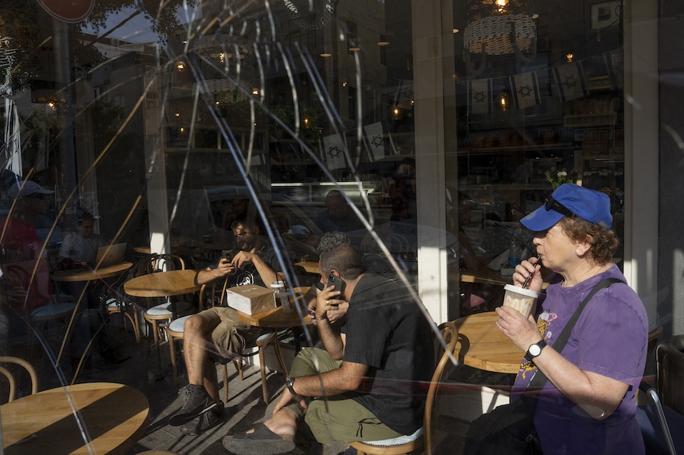 Una foto di lcuni cittadini di Tel Aviv all'interno di un bar la cui vetrina è stata incrinata a causa dell'attacco che ha colpito un palazzo residenziale vicino all'ambasciata americana, 19 luglio 2024 (AP Photo/Oded Balilty)