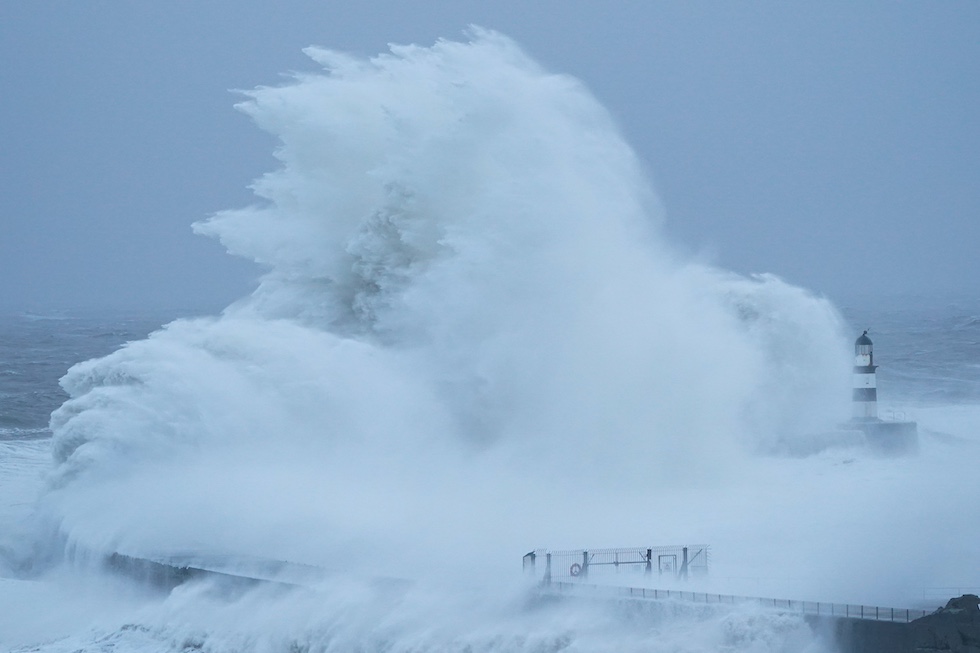 Gli schizzi di un'onda molto alta sovrastano il faro di un porto 