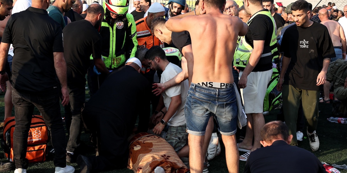 Personale dei servizi di emergenza e altre persone intorno nel campo da calcio colpito dal bombardamento (EPA/ATEF SAFADI)