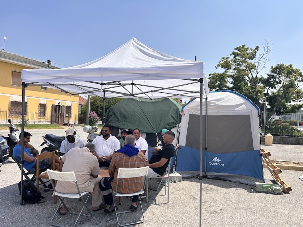 Un gruppo di lavoratori della ProSus seduti in cerchio sotto il gazebo montato davanti allo stabilimento.