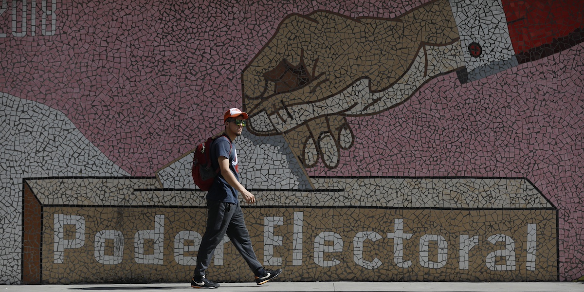 Un uomo cammina di fronte a un murales fuori dagli uffici del Consiglio elettorale nazionale a Caracas, Venezuela (AP Photo/Cristian Hernandez)