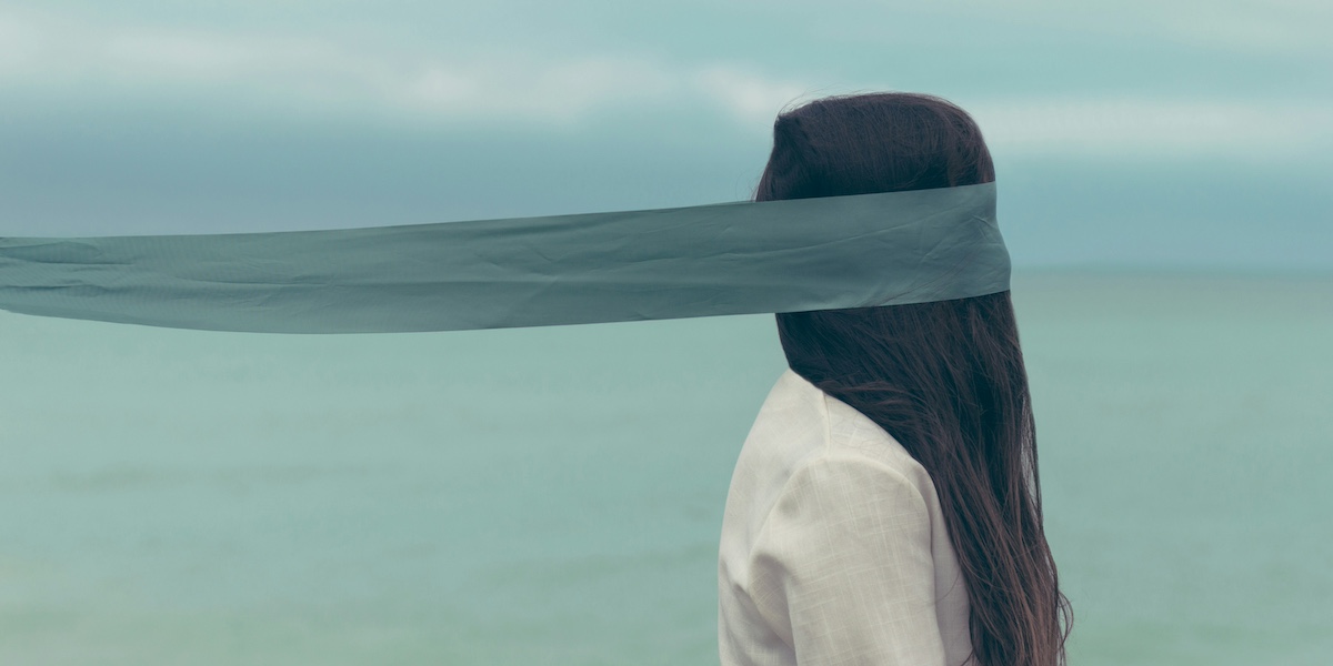 Una donna fotografata di profilo, con lunghi capelli che le coprono interamente il volto, e una benda intorno alla testa, all'altezza degli occhi