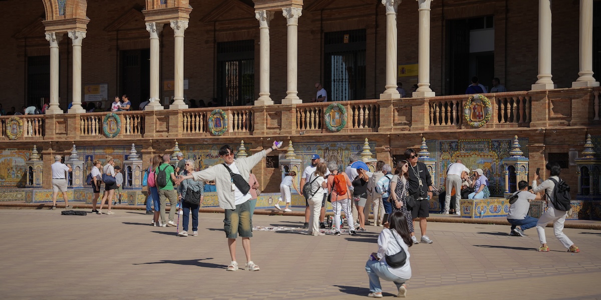 Turisti in Plaza de España a Siviglia; in primo piano una donna fotografa un uomo in posa