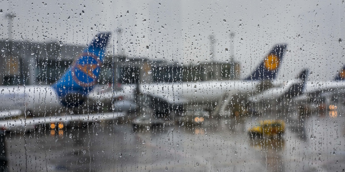 Alcuni aerei fermi in aeroporto, visti attraverso un vetro rigato dalle gocce di pioggia