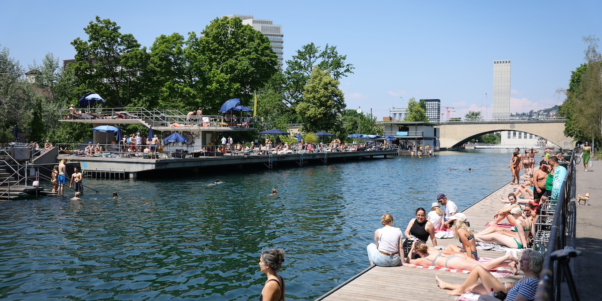 File di persone in costume sedute a prendere il sole lungo le rive del fiume