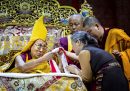 il dalai lama, con un alto copricapo giallo e affiancato da altri monaci, stringe la mano a una donna