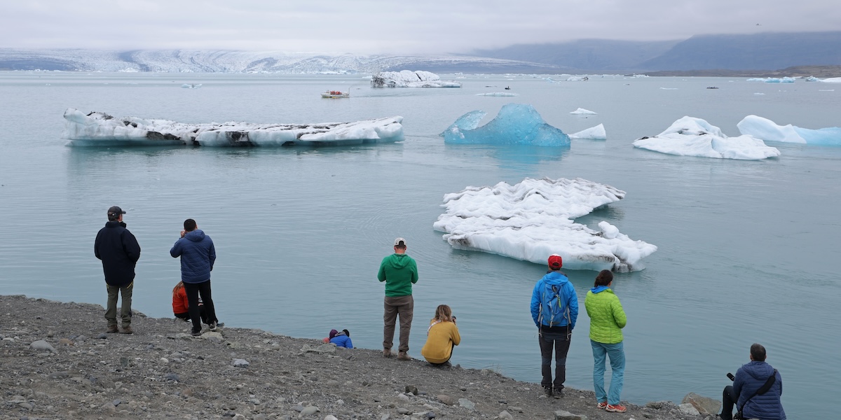 Un gruppo di turisti osserva dei pezzi di ghiaccio staccatisi dal ghiacciaio Breiðamerkurjökull (sullo sfondo) e galleggianti sul lago Jökulsárlón