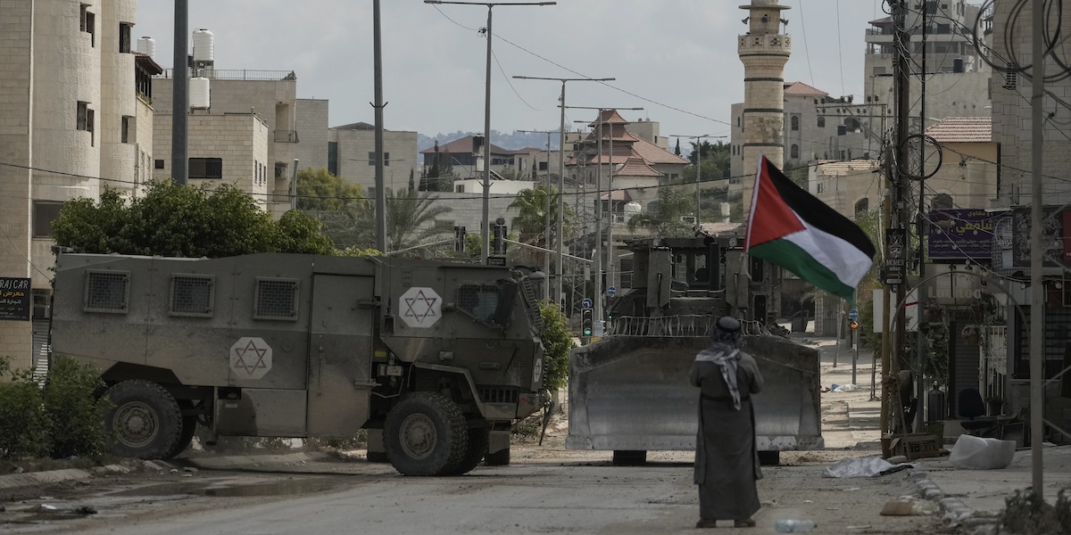 L'attivista Khairi Hanoon sventola una bandiera palestinese davanti a un convoglio militare israeliano a Tulkarem, in Cisgiordania, il 3 settembre 2024 (AP Photo/Majdi Mohammed)