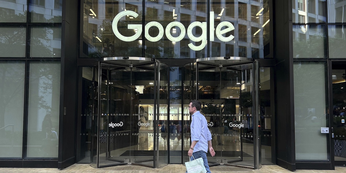 Un palazzo di vetro con l'insegna di google sopra la porta di ingresso e un uomo che ci cammina davanti