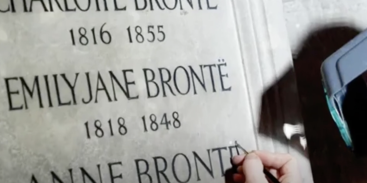 La restauratrice britannica Lucy Ackland corregge il nome delle sorelle Brontë sulla targa a loro dedicata all'abbazia di Westminster (dal canale YouTube DTX News)