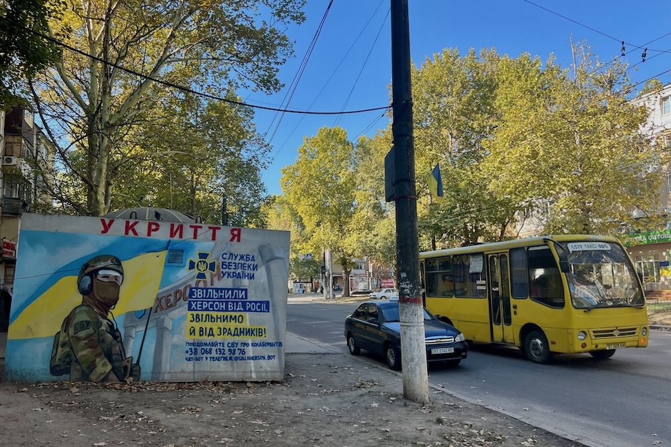 Foto di un bus municipale a Kherson e di una scritta su un muro che invita i cittadini a denunciare ai servizi segreti "i traditori che collaborano con la Russia" 