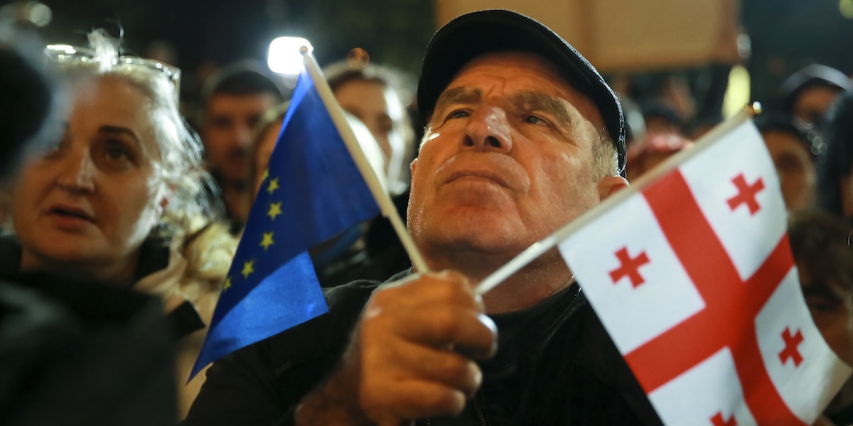 Un uomo con una bandierina della Georgia e una dell'Unione Europea durante una manifestazione contro i risultati delle elezioni a Tbilisi, lunedì 28 ottobre (AP Photo/ Zurab Tsertsvadze)