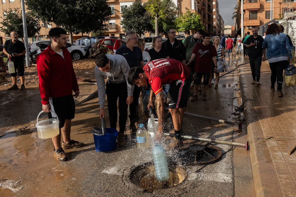 Persone in fila per prendere acqua potabile da una tubatura accessibile da un tombino