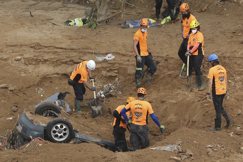 Un gruppo di persone attorno a un'automobile ribaltata e parzialmente sepolta