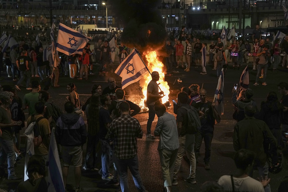 Un falò al centro di un gruppo di persone con delle bandiere israeliane