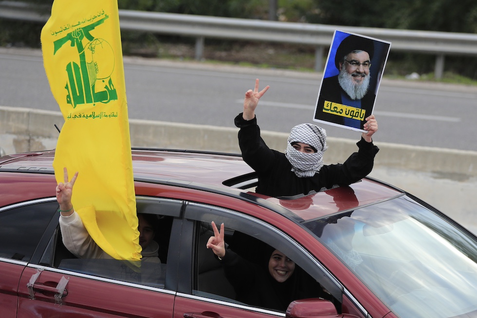 Passeggeri di un'auto in Libano mostrano la bandiera di Hezbollah e la foto dello storico leader del gruppo, Hassan Nasrallah, dopo l'annuncio del cessate il fuoco