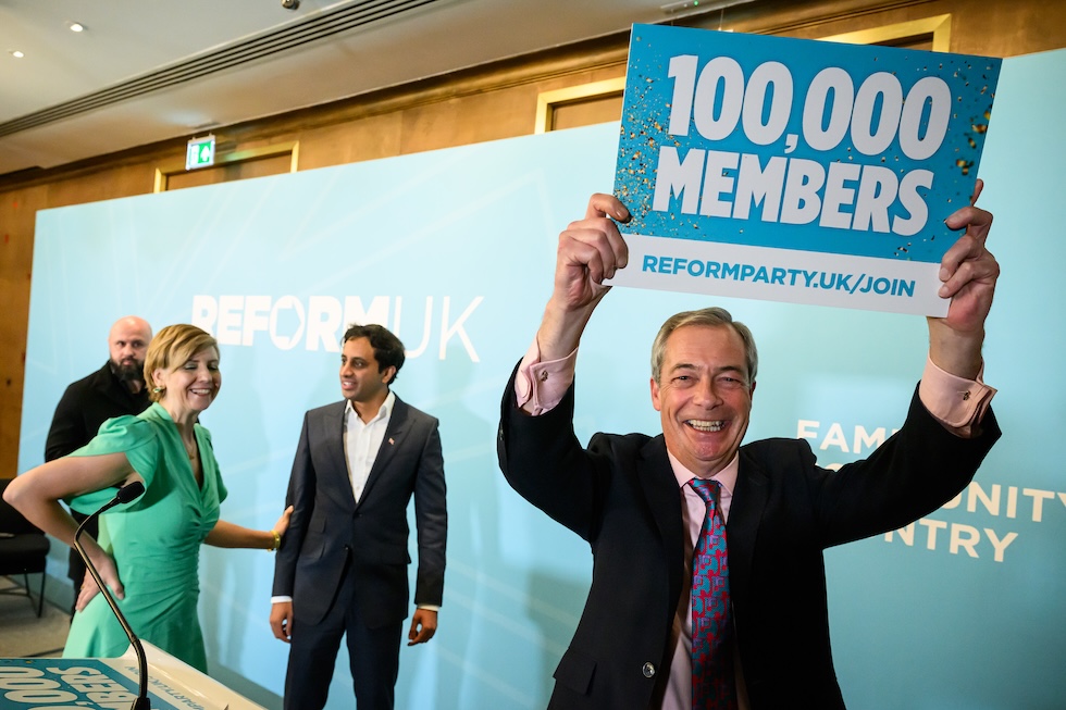 Nigel Farage con un cartello che celebra i 100mila tesserati di Reform UK, il 28 novembre