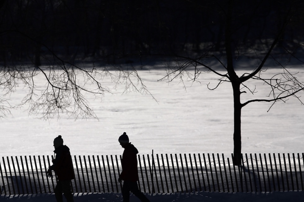 Due persone in controluce passeggiano lungo la riva di un lago