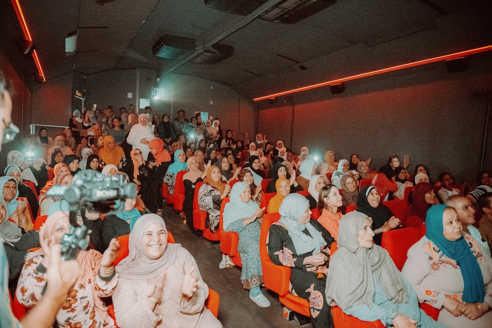 Donne che in larga parte indossano il velo e applaudiscono sedute in una piccola sala cinematografica