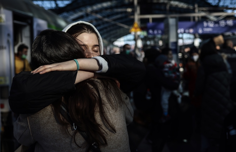 A girl with ⁢her eyes ⁢closed hugs another woman, framed⁣ from behind